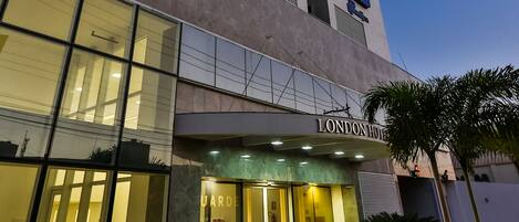 Een modern hotelgebouw met een opvallende entree, grote glasramen en een bordje met de tekst London Hotel.