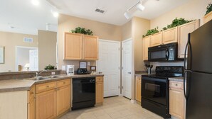 A modern kitchen with wooden cabinets, a black refrigerator, a microwave, an oven, and a dishwasher. - Disneys Den by VillaDirect (Davenport)