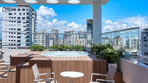 A rooftop terrace with a wooden deck, a hot tub, and seating area with chairs and a table. - PrivateTerrace-BlueMall-Jacuzzi-AC-YellowKey (Santo Domingo)