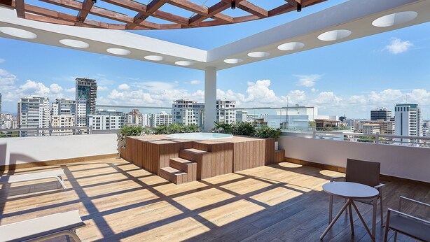 A rooftop terrace with a wooden deck, a hot tub, and a seating area with a table and chairs. - PrivateTerrace-BlueMall-Jacuzzi-AC-YellowKey (Santo Domingo)