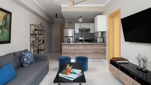 A modern living room with a grey sofa, blue ottomans, a black coffee table with a book, and a flat-screen TV mounted on the wall. - PrivateTerrace-BlueMall-Jacuzzi-AC-YellowKey (Santo Domingo)