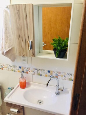 A bathroom with a white sink, a mirror, a towel hanging on the wall, and a potted plant.