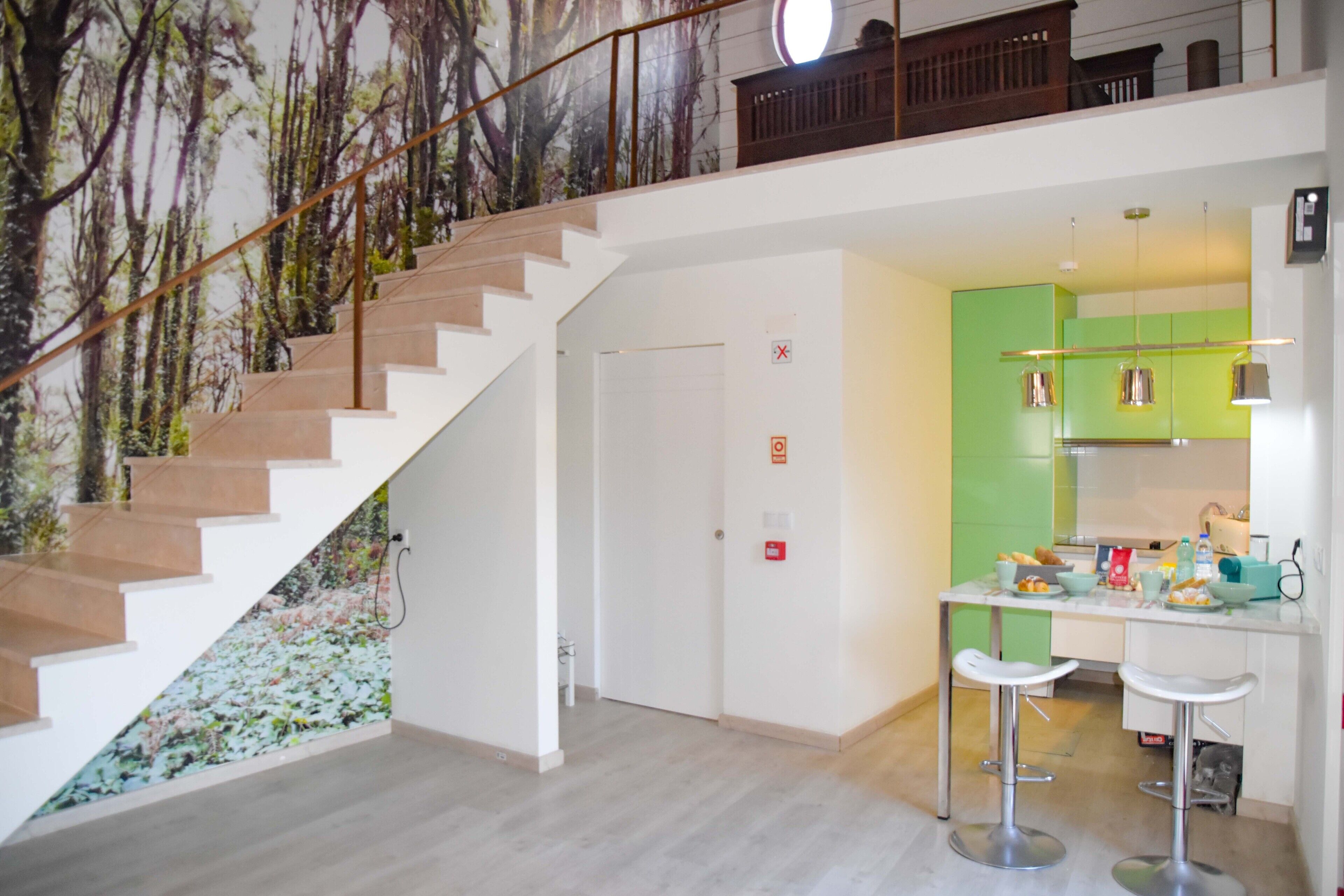 A modern interior with a staircase, a kitchen area with green cabinets, and a dining bar with stools.