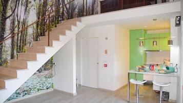 A modern interior with a staircase, a kitchen area with green cabinets, and a dining bar with stools.