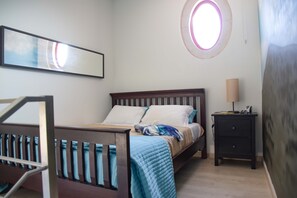 Un dormitorio con cama, mesita de noche, lámpara, ventana con vistas y un cuadro en la pared.