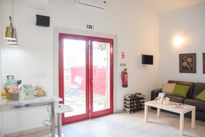 Una sala de estar moderna con una puerta corredera de marco rojo, una mesa de centro blanca, un sofá de cuero negro con cojines verdes, un televisor de pantalla plana montado en la pared y una estantería para vinos.