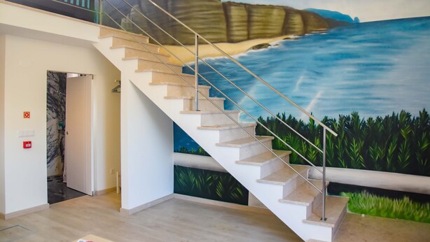 A staircase with a mural of a coastal landscape, a handrail, and a door leading to another room. - Tia Malaca (Sintra)