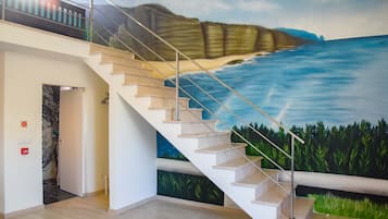 A staircase with a mural of a coastal landscape, a handrail, and a door leading to another room.