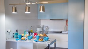 A modern kitchen with light blue cabinets, a stainless steel refrigerator, and a dining area with a table and bar stools. - Tia Malaca (Sintra)