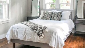 Une chambre à coucher avec un lit, un plancher en bois, un ventilateur de plafond et deux fenêtres.