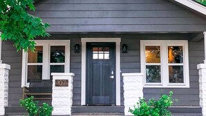 Une maison avec une porte d’entrée sombre, deux fenêtres de chaque côté et le numéro « 107 » sur le mur avant.