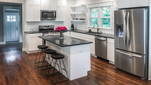 Une cuisine moderne avec des meubles blancs, un îlot central, des appareils en acier inoxydable et un plancher en bois foncé.