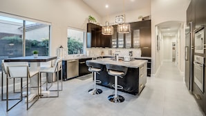 A modern kitchen with a large island, bar stools, and pendant lighting. - Recently Renovated Luxury Home in Grayhawk (Scottsdale)