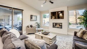 A spacious living room with a large sofa, a coffee table, and a fireplace. There is a ceiling fan, large windows, and a view of the outside. - Recently Renovated Luxury Home in Grayhawk (Scottsdale)