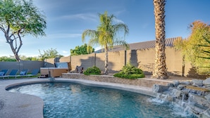 A swimming pool with a waterfall feature, surrounded by palm trees and a brick wall. - Recently Renovated Luxury Home in Grayhawk (Scottsdale)