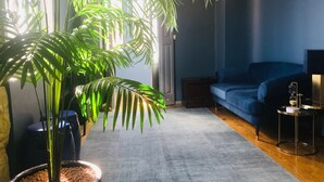 A living room with a large potted plant, a blue sofa, a small side table, and a lamp. - ★ Romantic - Casa Bela ★ Penthouse with views (Porto)