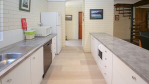 Ett modernt kök med vita skåp, en diskho i rostfritt stål, en mikrovågsugn och en diskmaskin. På väggen hänger en brandsläckare och ovanför mikrovågsugnen finns en inramad tavla.