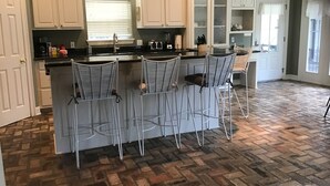 A kitchen with white cabinets, a herringbone-patterned floor, and three bar stools.