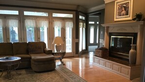 A living room with a sectional sofa, a coffee table, a fireplace, and a large window with curtains.