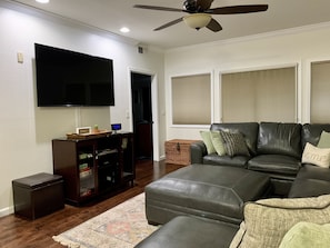 A living room with a flat-screen TV, leather sofa, and a ceiling fan.