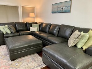 A modern living room with a sectional sofa, ottoman, patterned rug, and a painting of sailboats.