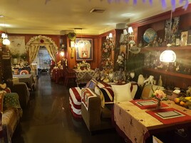 A cozy hotel lobby with a central seating area, a dining table with a red table runner, and a variety of decorative items and furniture.