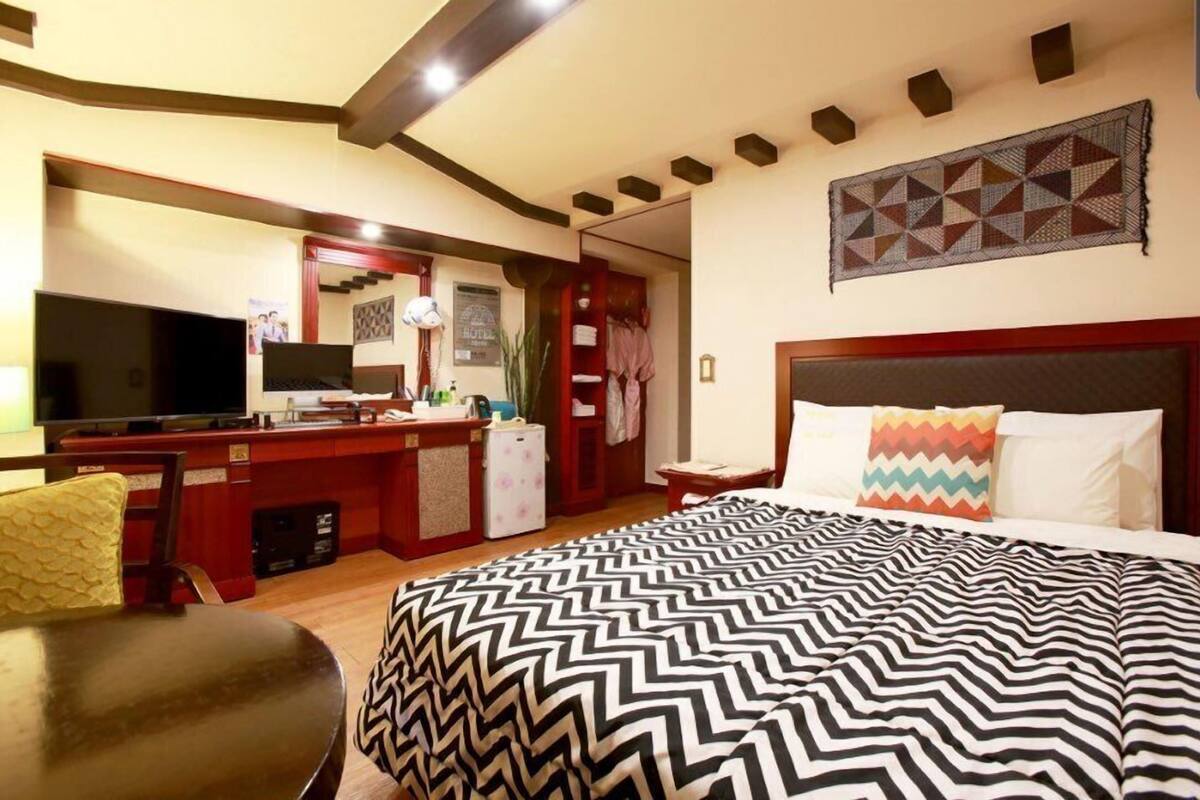 A hotel room with a bed, a desk, a television, and a small kitchenette.