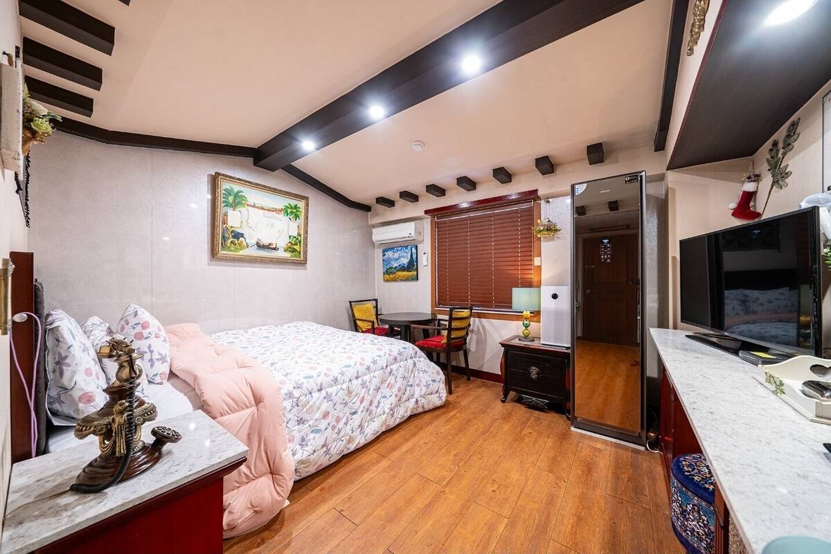 A hotel room with a bed, a desk, a TV, and a window with blinds.