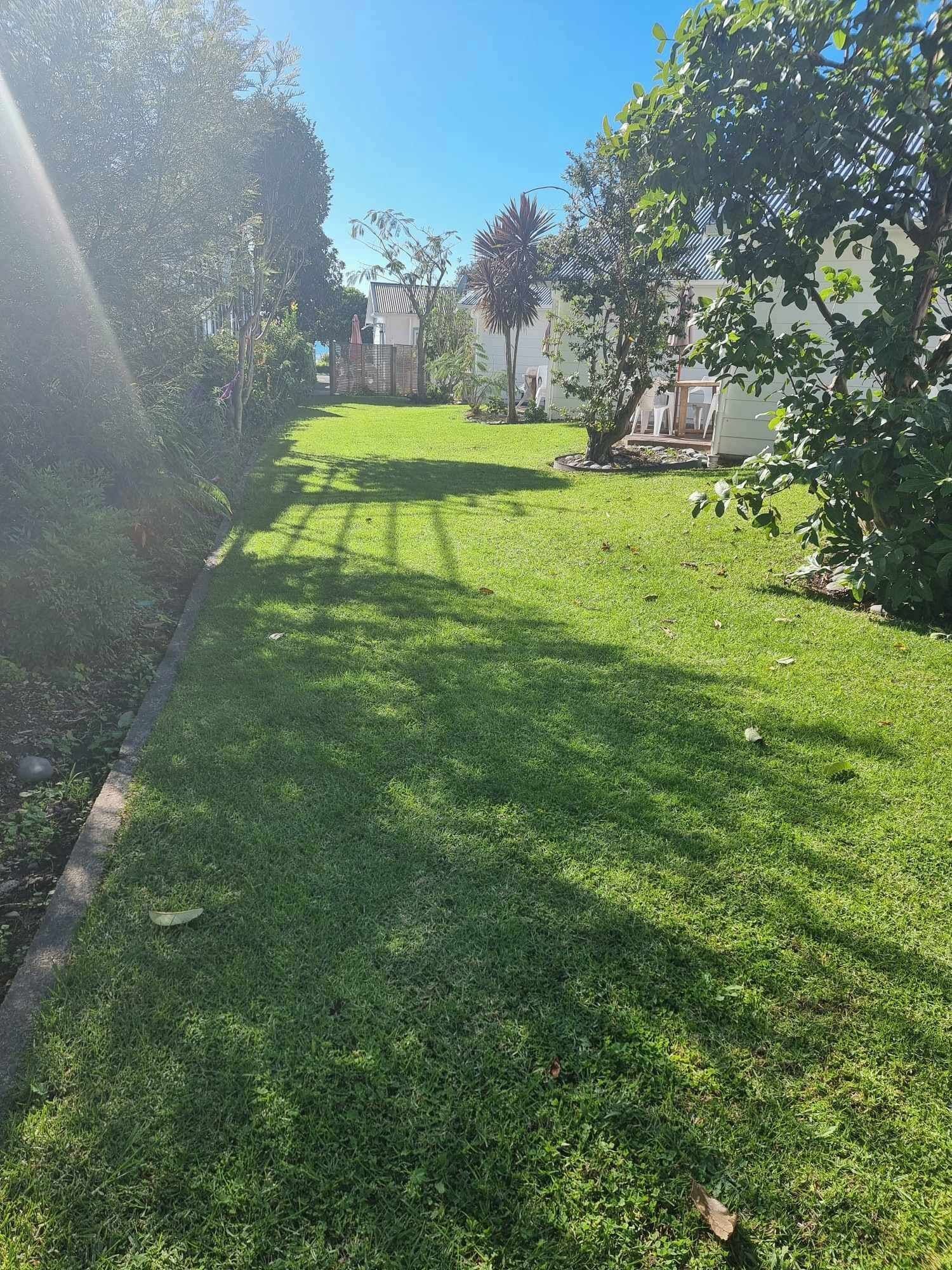 Zona verde y bien cuidada, con cielo despejado, rodeada de árboles y una valla.