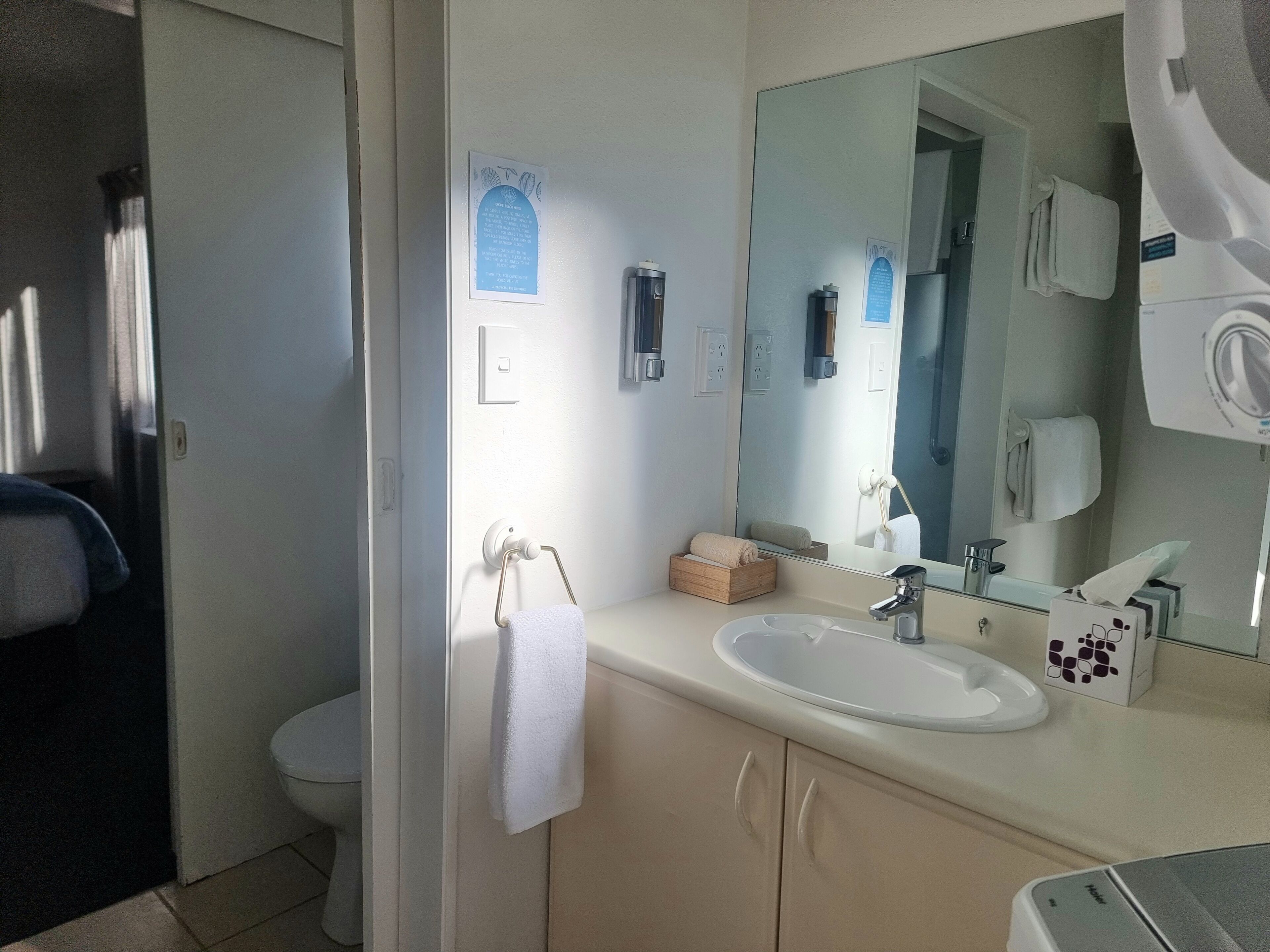 Ein Badezimmer mit Waschbecken, Spiegel, Handtuchhalter und einer kleinen Holzkiste.