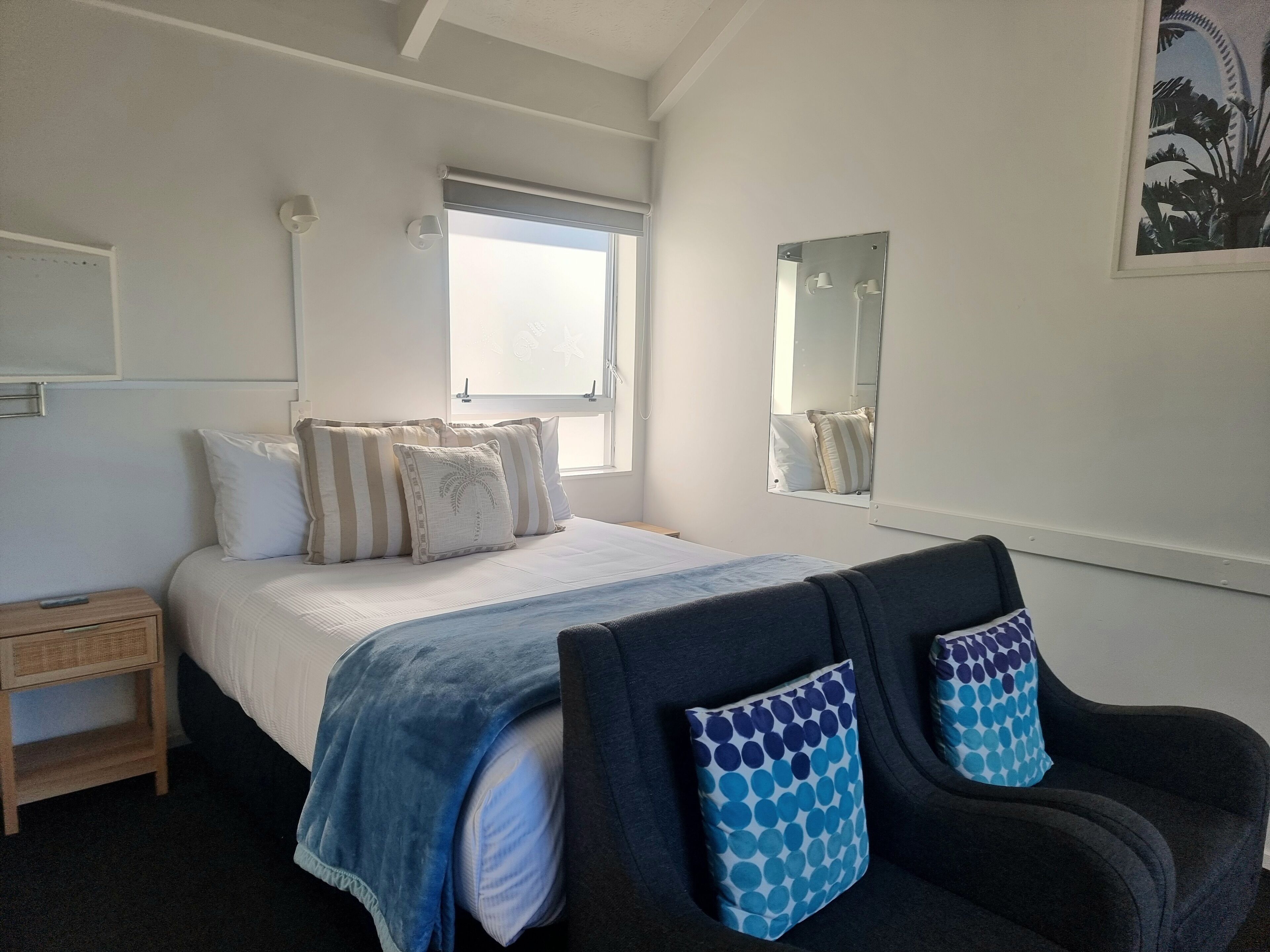 A bedroom with a bed, bedside table, nightstand, and a window with a view.