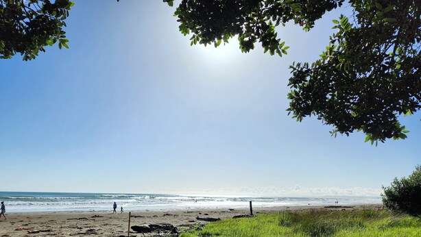 A beach with a clear sky, calm sea, and people walking. - Ohope Beach Motel (Ohope)