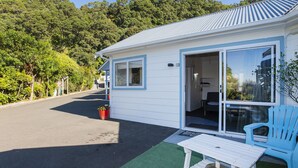 A small, single-story building with a white exterior and blue trim. It features a sliding glass door entrance, a small porch area, and a seating area with a table and chairs. - Ohope Beach Motel (Ohope)