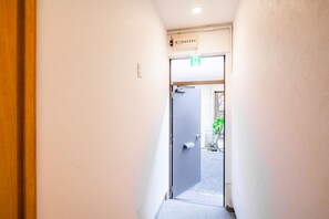 A narrow hallway with a door at the end leading outside. - Sakuragawa no Waho House (Osaka)