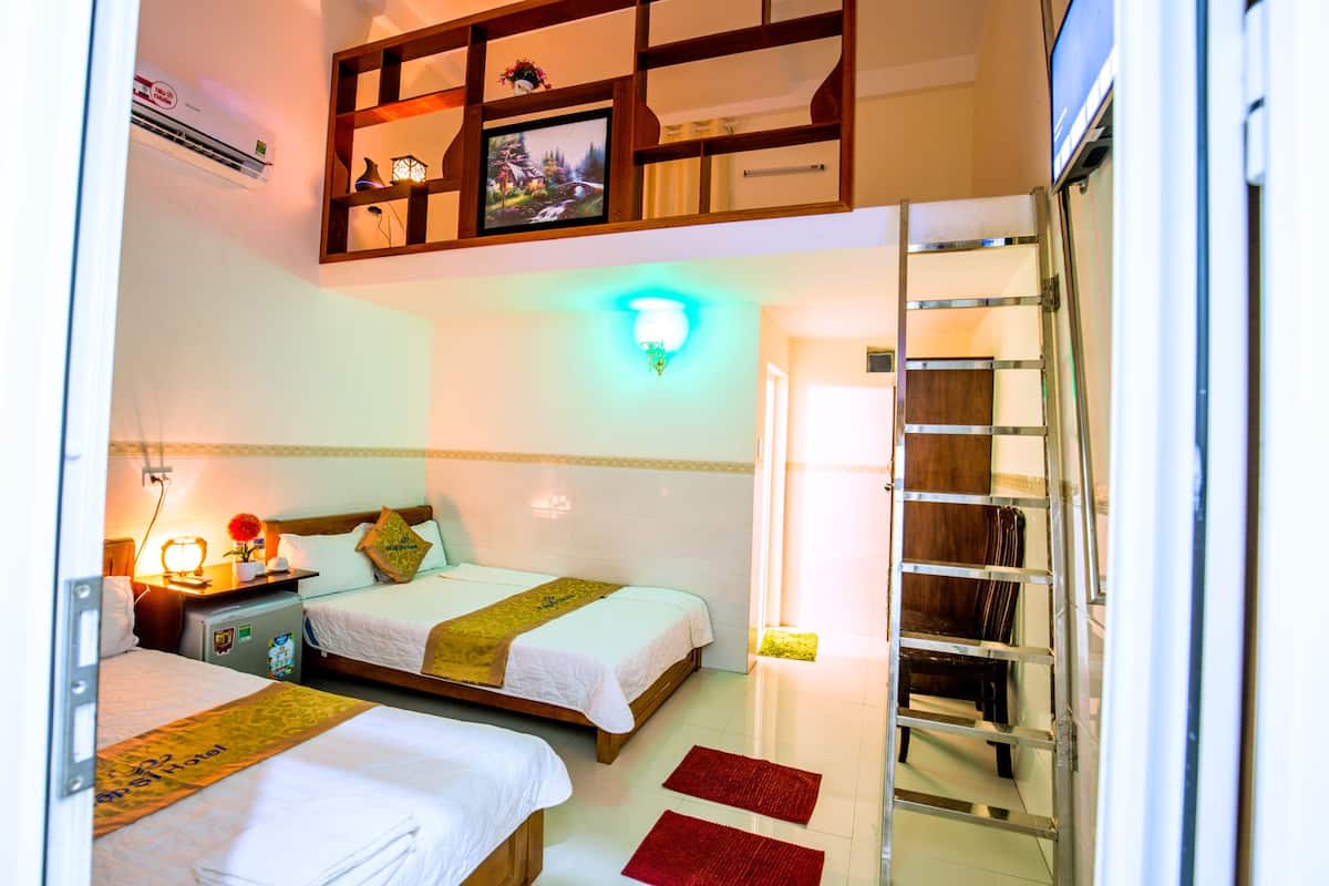 A hotel room with two beds, a desk with a lamp, a wall-mounted TV, and a shelf with decorative items.