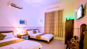 Une chambre d’hôtel avec deux lits, une télévision, une armoire et un bureau avec une lampe et des fleurs.