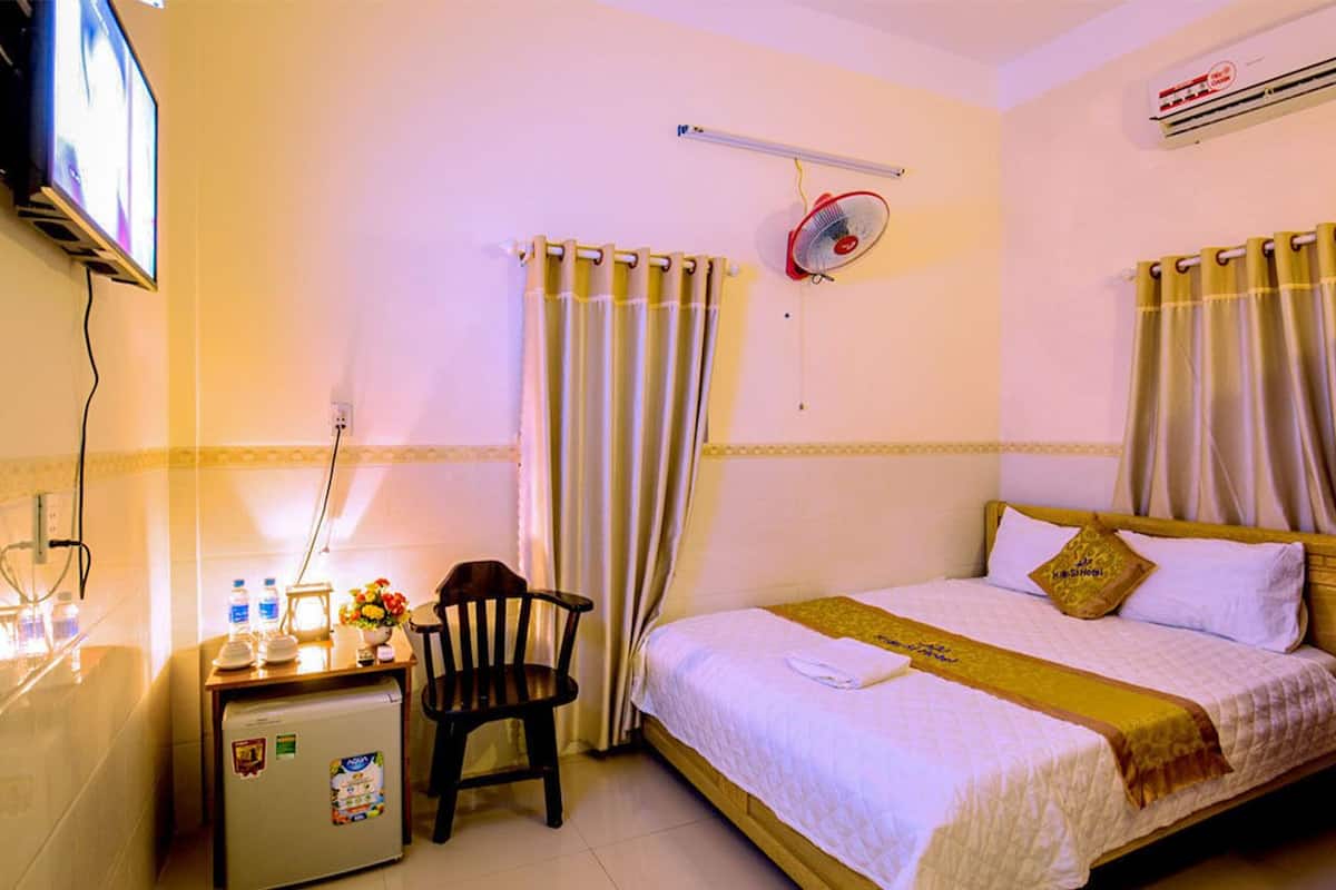 A hotel room with a bed, a desk with a refrigerator, a chair, a TV, and curtains.