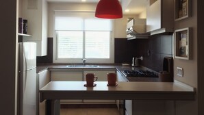 Une cuisine moderne avec un îlot central, une fenêtre et un luminaire suspendu rouge.