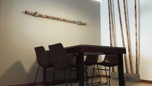 Un coin repas comprenant une table rectangulaire, quatre chaises, une étagère fixée au mur et des tiges de bambou.