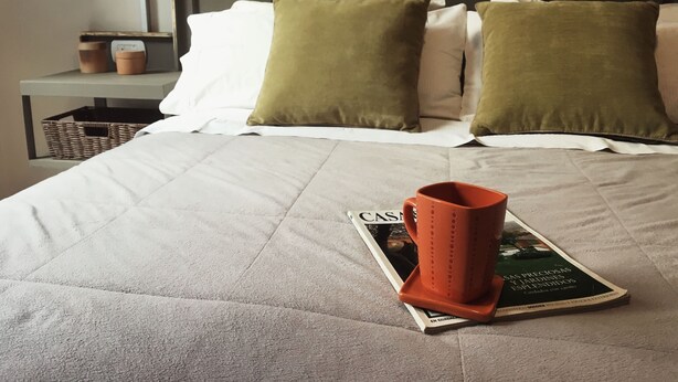 Un lit bien fait, avec une couverture matelassée, deux oreillers et un magazine posé sur le lit.