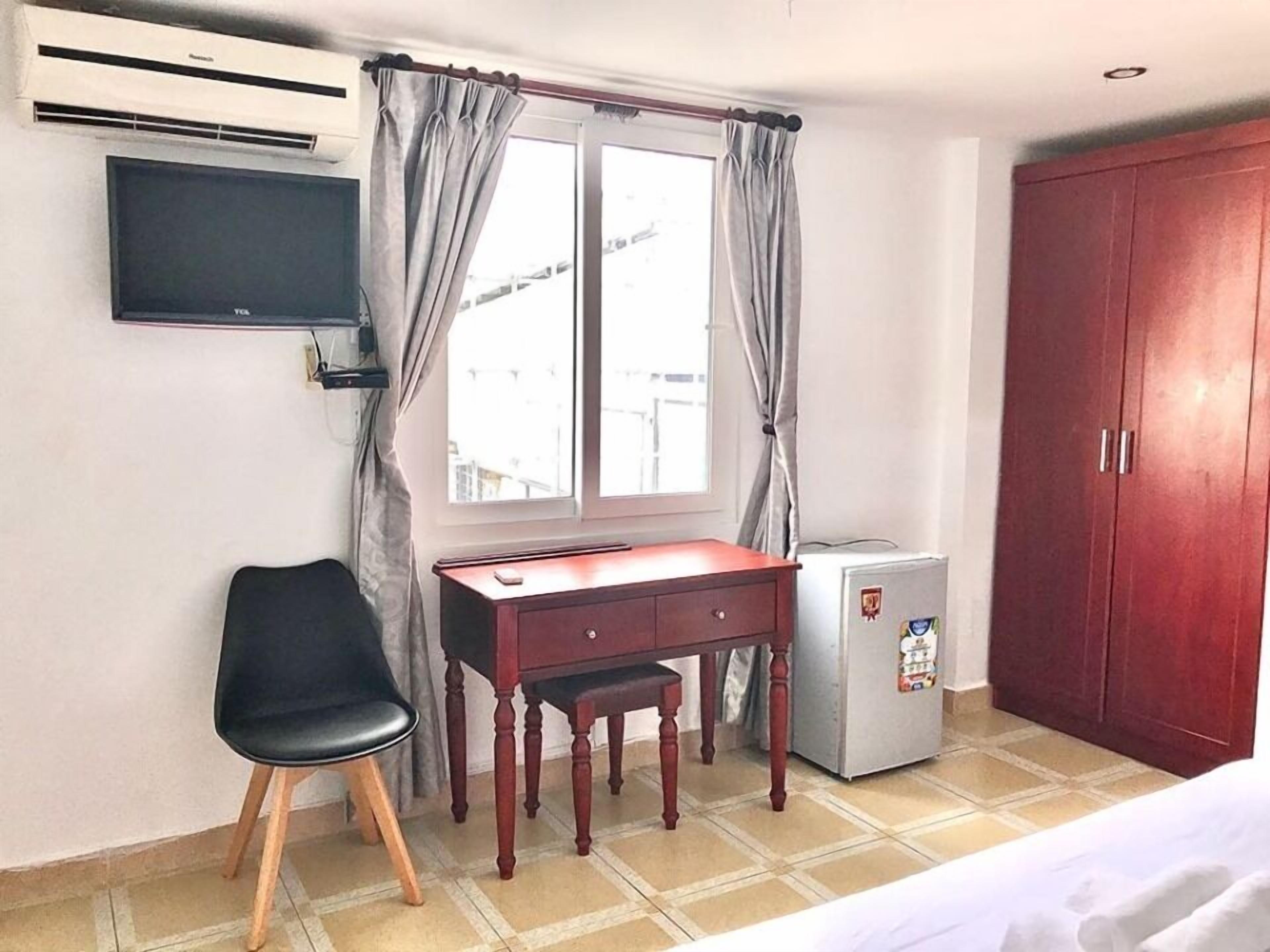 A room with a desk, chair, wardrobe, and a small refrigerator.