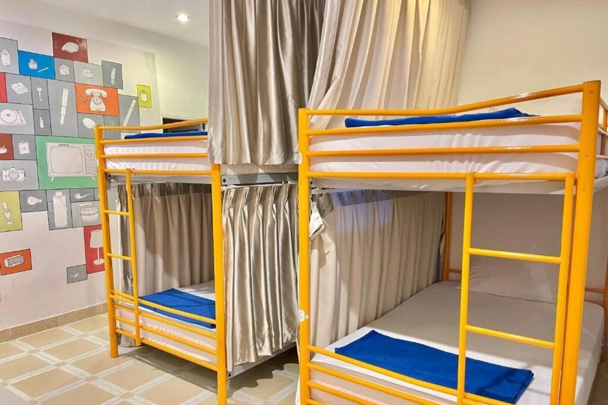 Two bunk beds with yellow frames and blue bedding, a curtain, and a wall with various icons.