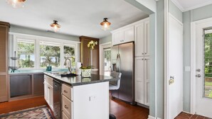 A modern kitchen with white cabinets, a stainless steel refrigerator, and a large island with a sink. - Waterfront “State of Mind” vintage home.  (Bluffton)