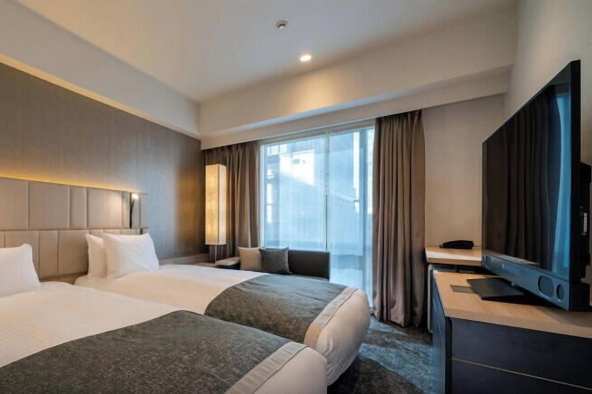 Een hotelkamer met twee bedden, een televisie, een bureau en een groot raam met gordijnen.
