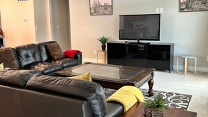 Een woonkamer met een leren bank, een salontafel met glazen blad, een flatscreen televisie en een kleine plant op een bijzettafeltje.