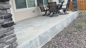 Een huis met een overdekte patio, voorzien van een stenen muur, een betonnen vloer en een zithoek met stoelen en een tafel.