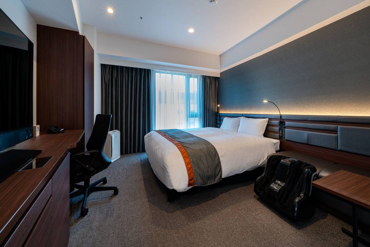 Una habitación de hotel moderna con una cama grande, un escritorio, una silla y una maleta.