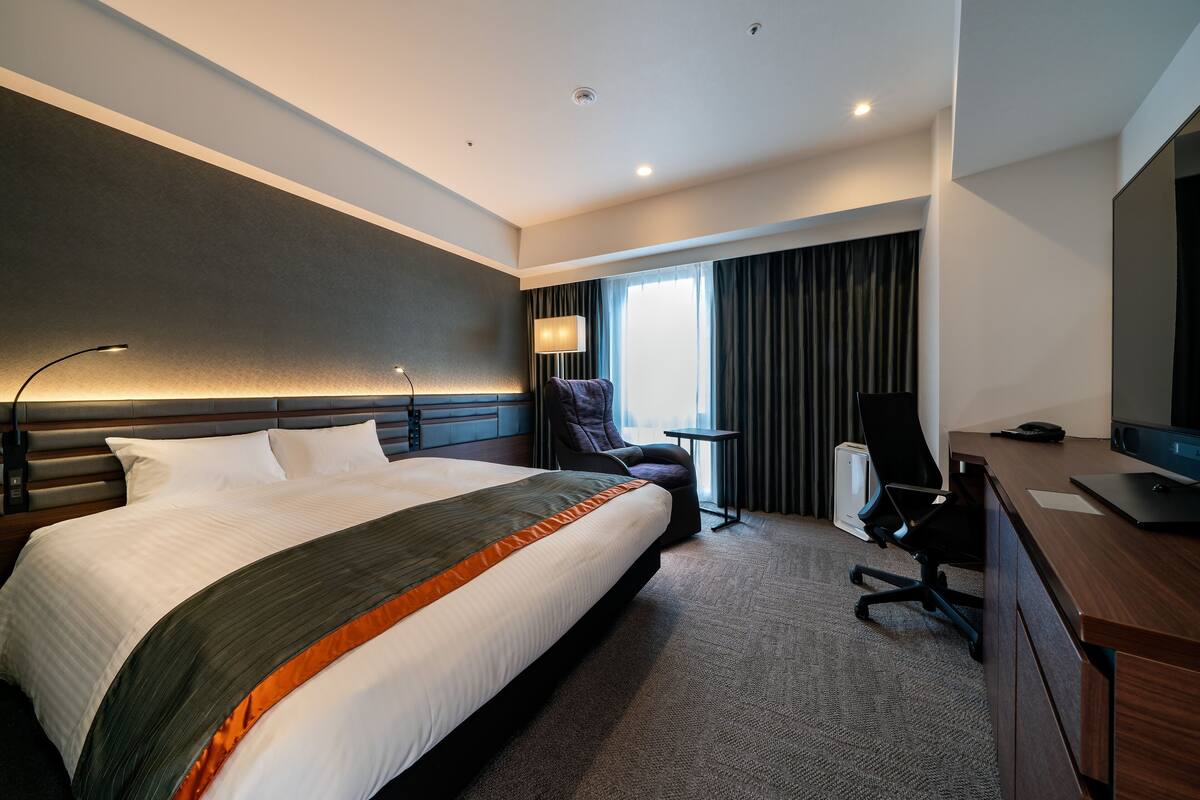 Una habitación de hotel moderna con una cama grande, un escritorio, una silla y un televisor.