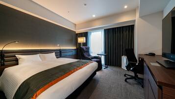 A modern hotel room with a large bed, a desk, a chair, and a TV.