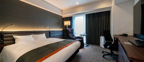 A modern hotel room with a large bed, a desk, a chair, and a TV.